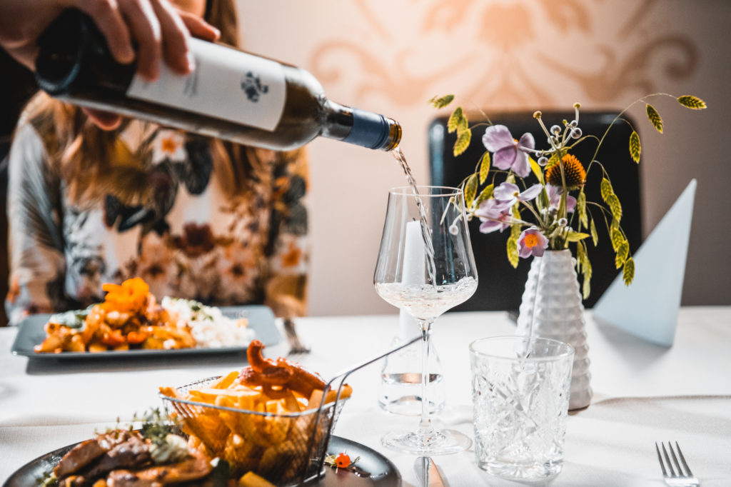 Geheimtipp Restaurant in der Südsteiermark. Es wird gerade ein in ein Weinglas geschehnkt. Der Tisch ist wunderschön floral gedeckt